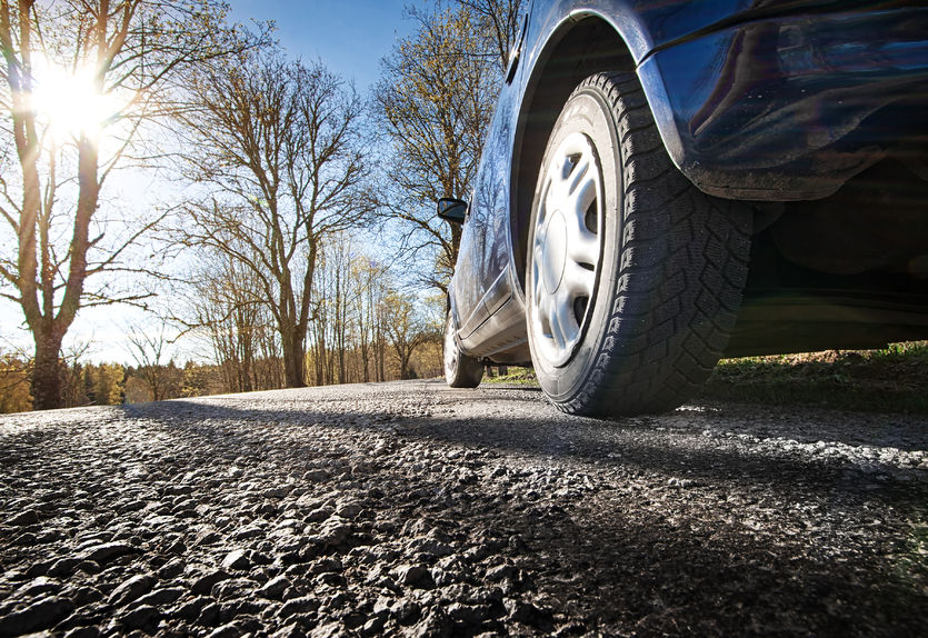 low view of a car tire driving down gravel road