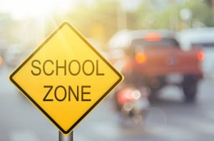 School zone warning sign on blur traffic road with colorful bokeh light abstract background.
