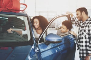 African american family at car dealership. Father, mother and son near new car.